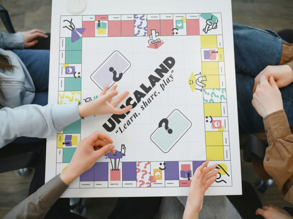 Studenti che giocano al gioco da tavolo Unicaland durante un'attività di socializzazione e condivisione negli spazi comuni della residenza universitaria.
